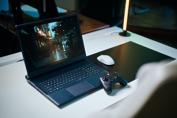 En öppen Alienware-speldator uppställd på ett vitt studiobord, där en mörk, reflekterande gatumiljö visas i skarpa, path-traced detaljer, tillsammans med en svart handkontroll och en vit trådlös mus.