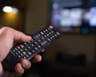Hand som håller en fjärrkontroll med en suddig TV i bakgrunden