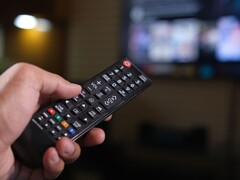 Hand som håller en fjärrkontroll med en suddig TV i bakgrunden