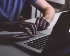 Händer som skriver på ett MacBook-tangentbord i svagt ljus, med Apples logotyp som lyser