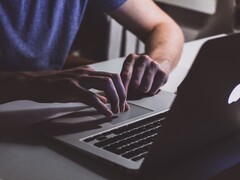 Händer som skriver på ett MacBook-tangentbord i svagt ljus, med Apples logotyp som lyser