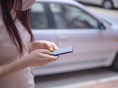 En kvinna som skriver på sin smartphone med en silverfärgad bil i bakgrunden