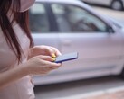 En kvinna som skriver på sin smartphone med en silverfärgad bil i bakgrunden