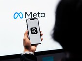 En hand håller en smartphone framför en stor Meta-logotyp