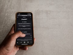 Hand som håller en smartphone som visar ChatGPT-gränssnittet ovanför en grå stenyta