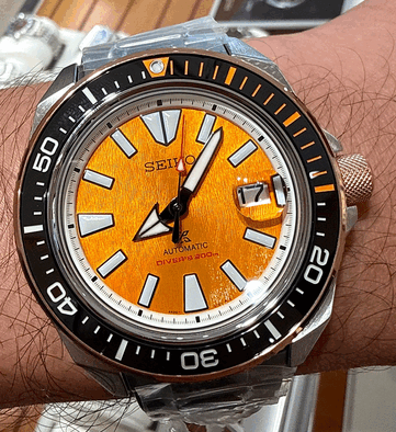 Närbild på Seiko Prospex HBB005K1 som visar dess strukturerade bärnstensfärgade urtavla, extra stora självlysande timmarkeringar, breda visare, datumfönster och svart dykkrans med orange markeringar.