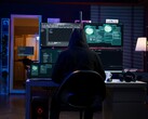 En forskare med huva arbetar över flera skärmar i en mörk miljö. Generisk hackare på bilden.
