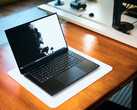 En öppen, matt svart Razer Blade 16-speldator som står på en vit skrivbordsmatta ovanpå ett varmt träbord, med en livfull svartvit bakgrundsbild.