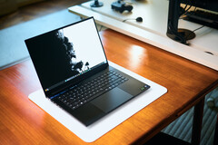 En öppen, matt svart Razer Blade 16-speldator som står på en vit skrivbordsmatta ovanpå ett varmt träbord, med en livfull svartvit bakgrundsbild.