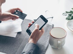 Person som trycker på en smartphone medan hen håller ett bankkort i den andra handen