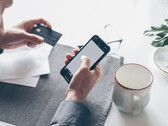 Person som trycker på en smartphone medan hen håller ett bankkort i den andra handen