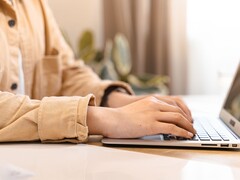 Händer som skriver på tangentbordet på en öppen bärbar dator vid ett ljust skrivbord