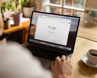 Person vid en bärbar dator med Googles startsida öppen, bredvid en kopp kaffe