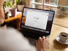 Person vid en bärbar dator med Googles startsida öppen, bredvid en kopp kaffe