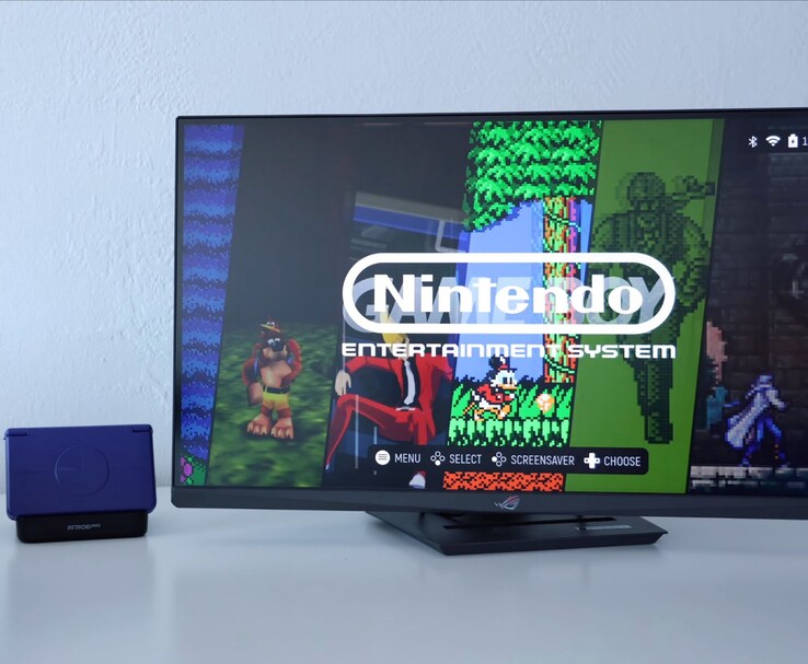 Retroid Pocket Flip 2 i lila placerad på en docka bredvid en bildskärm, med TV-skärmen som visar ett retro NES-emulatorgränssnitt. (Bildkälla: Retro Game Corps på YouTube)