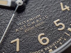 Närbild på Timex Expedition Field Post Titaniums strukturerade svarta urtavla med arabiska siffror, självlysande visare och markörer samt datumfönster.