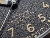 Närbild på Timex Expedition Field Post Titaniums strukturerade svarta urtavla med arabiska siffror, självlysande visare och markörer samt datumfönster.