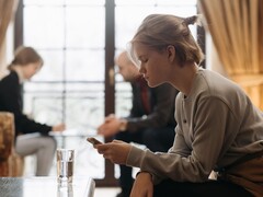 En tonåring tittar på sin smartphone, medan två vuxna sitter oskarpa i bakgrunden.