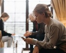 En tonåring tittar på sin smartphone, medan två vuxna sitter oskarpa i bakgrunden.