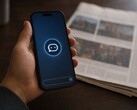 En hand håller en smartphone med en chatbot-ikon, och bredvid den ligger en tryckt tidning.