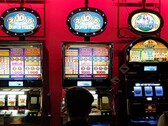 Spelautomater inne på ett kasino med starkt upplysta skärmar och människor som spelar framför (Bildkälla: djedj via Pixabay)