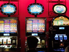 Spelautomater inne på ett kasino med starkt upplysta skärmar och människor som spelar framför (Bildkälla: djedj via Pixabay)