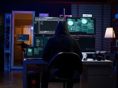 Figur med huva vid en installation med flera skärmar som kör en cyberattack. 