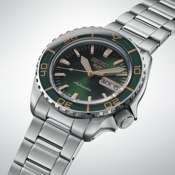 Närbild av Seiko 5 Sports SKX HDB005, som framhäver dess mörkgröna urtavla, roséguldfärgade visare och applicerade index samt matchande gröna vridring med guldfärgade markeringar.