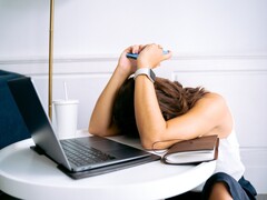 Kvinna som tittar ner på sin smartphone med en bärbar dator bredvid sig