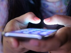 Två händer håller en smartphone med en lysande skärm i det svaga ljuset