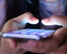 Två händer håller en smartphone med en lysande skärm i det svaga ljuset