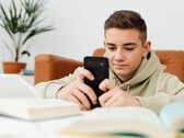 Tonåring i huvtröja som skriver på en smartphone med öppna skolböcker framför sig