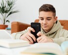 Tonåring i huvtröja som skriver på en smartphone med öppna skolböcker framför sig