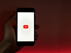 En hand som håller en smartphone med YouTube-logotypen upplyst på skärmen mot en röd bakgrund