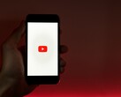 En hand som håller en smartphone med YouTube-logotypen upplyst på skärmen mot en röd bakgrund