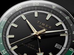 Närbild av Timex Atelier GMT Première M1a:s svarta urtavla med guldfärgade visare, självlysande timmarkörer, datumfönster och en svart och grön 24-timmars GMT-ring.