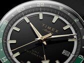 Närbild av Timex Atelier GMT Première M1a:s svarta urtavla med guldfärgade visare, självlysande timmarkörer, datumfönster och en svart och grön 24-timmars GMT-ring.