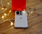 En OnePlus 15 ligger på ett träbord omgiven av varma ljusslingor, med en knallröd OnePlus-förpackning i bakgrunden.