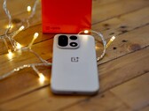 En OnePlus 15 ligger på ett träbord omgiven av varma ljusslingor, med en knallröd OnePlus-förpackning i bakgrunden.