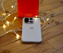 En OnePlus 15 ligger på ett träbord omgiven av varma ljusslingor, med en knallröd OnePlus-förpackning i bakgrunden.