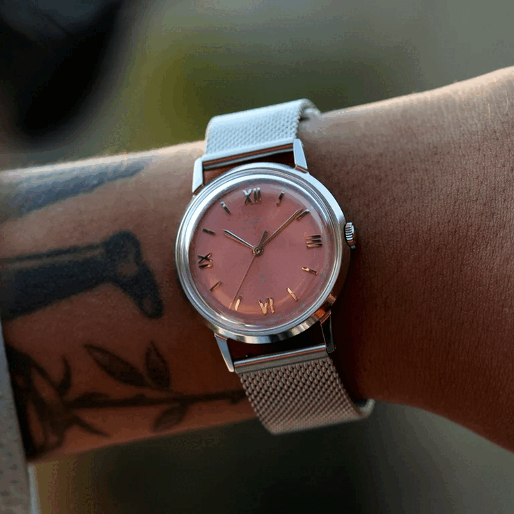 Person som bär Timex x Todd Snyder Marlin Mesh med en laxrosa urtavla med solstrålemönster och armband i nät.