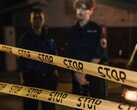 Två poliser står på natten bakom ett gult band med texten Stop