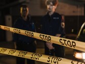 Två poliser står på natten bakom ett gult band med texten Stop