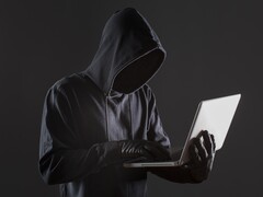 En hacker med huva som använder en bärbar dator mot en mörk bakgrund.