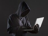 En hacker med huva som använder en bärbar dator mot en mörk bakgrund.