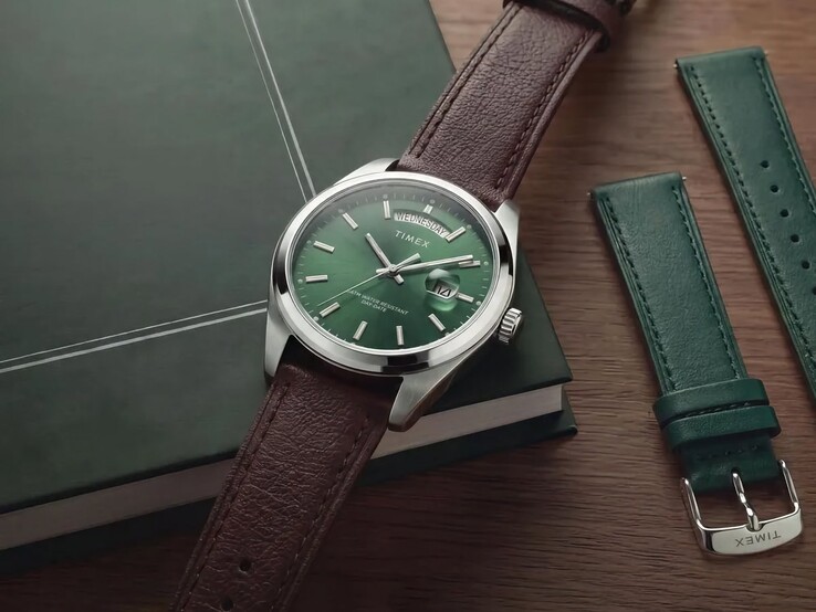 Timex Legacy Day and Date med sin gröna urtavla och bruna läderrem, placerad på en mörkgrön bok bredvid den utbytbara gröna läderremmen.