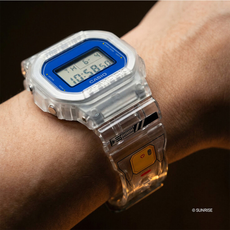 Casio G-Shock x Mobile Suit Gundam DW-5600GM26-7DR bärs på handleden, med ett transparent hartsfodral och armband, blå bezelomfattning och Gundam-inspirerad grafik på armbandet.
