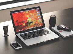 MacBook Pro på ett mörkt skrivbord bredvid en smartphone, glasögon och en anteckningsbok
