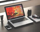 MacBook Pro på ett mörkt skrivbord bredvid en smartphone, glasögon och en anteckningsbok