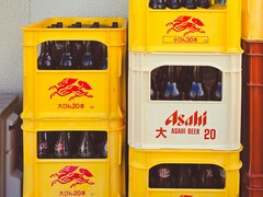 Staplade gula och vita plastbackar fyllda med Asahi-ölflaskor med japansk text och röda logotyper. (Bildkälla: Foto av Alazne Lazcano via Pexels)